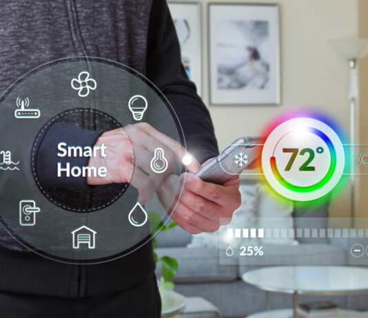 Mann hält ein iphone vor einem Haus während sie die Heizung mit Smart Home App steuert